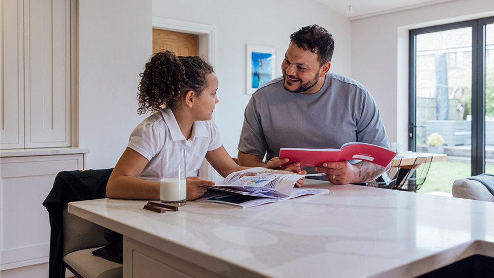 a father helping his daughter do her homework at the kitchen bench
