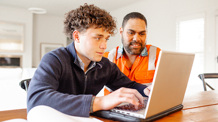 Teenage boy working on a laptop with an adult sitting beside him.