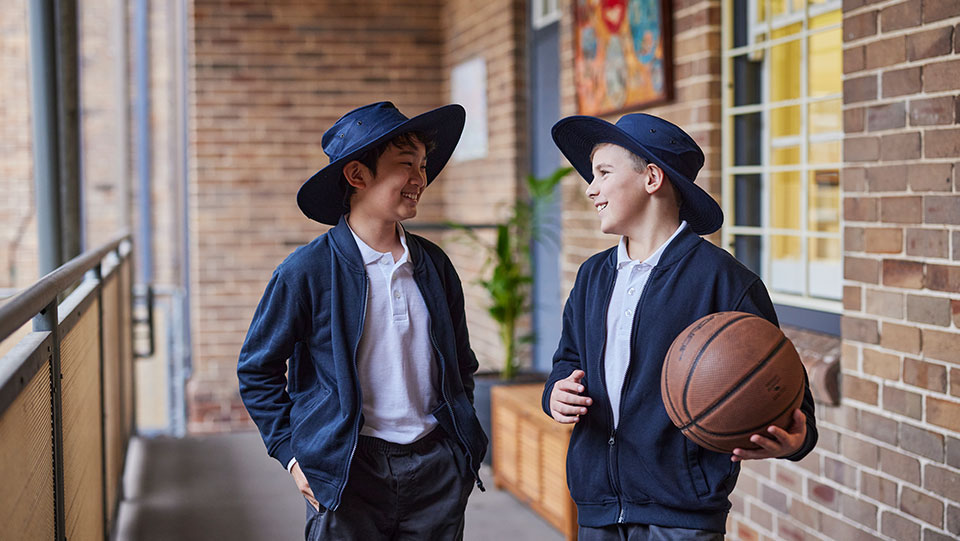 two school kids talking to each other, the school boy on the right is holding a basketball in his left hand