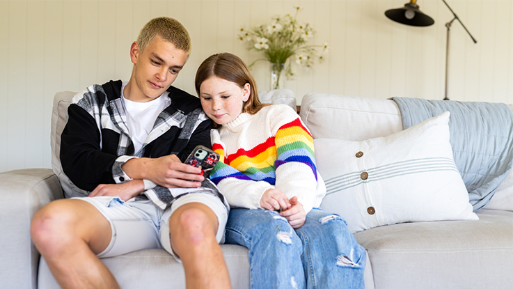 Teenage boy and girl sitting on a couch looking at a smartphone together.