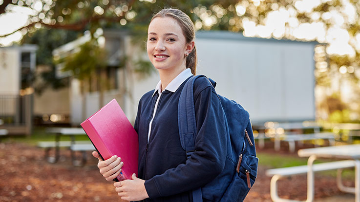 a school girl in high school carrying a pink folder and a blue backpack