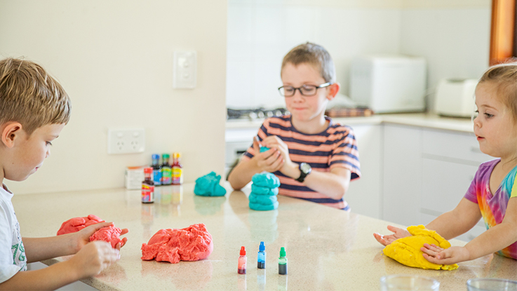 Three children sitting at a table indoors, playing with colourful modelling clay.