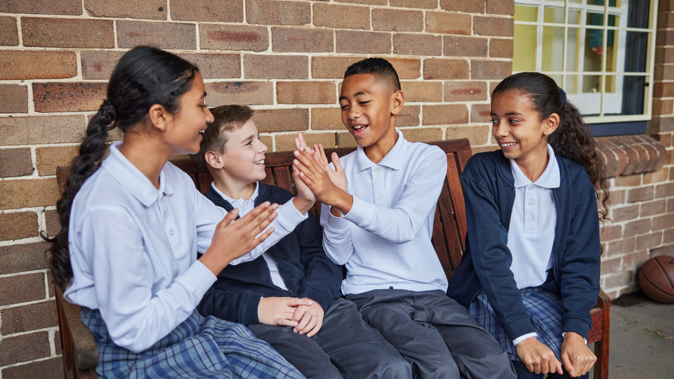 school kids sitting on a wooden bench playing