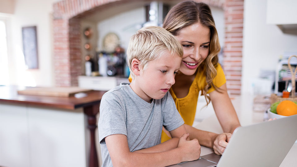 a mother wearing a yellow top is on the laptop with her son checking his school report