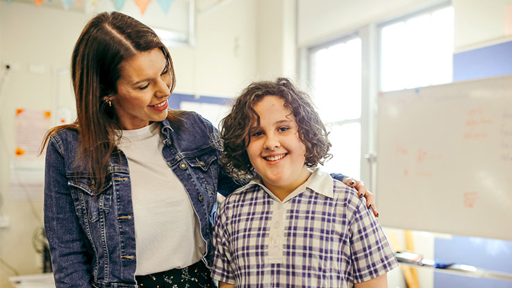 a school girl smiling in the classroom with a guardian next to her