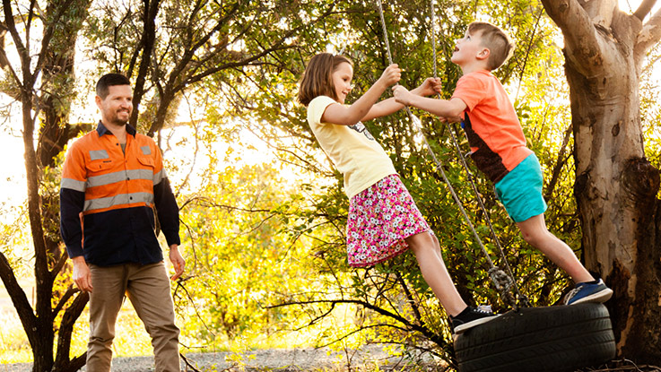 two kids are playing on a tyre swing while their father watches