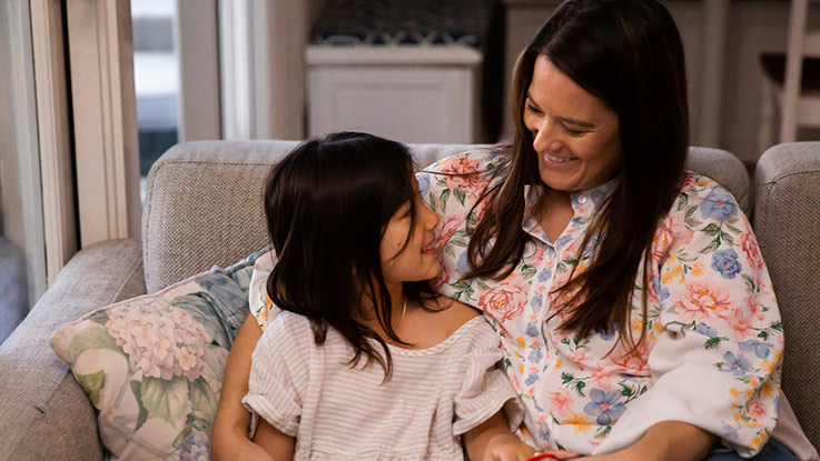 a mother sitting with her daughter smiling on the couch