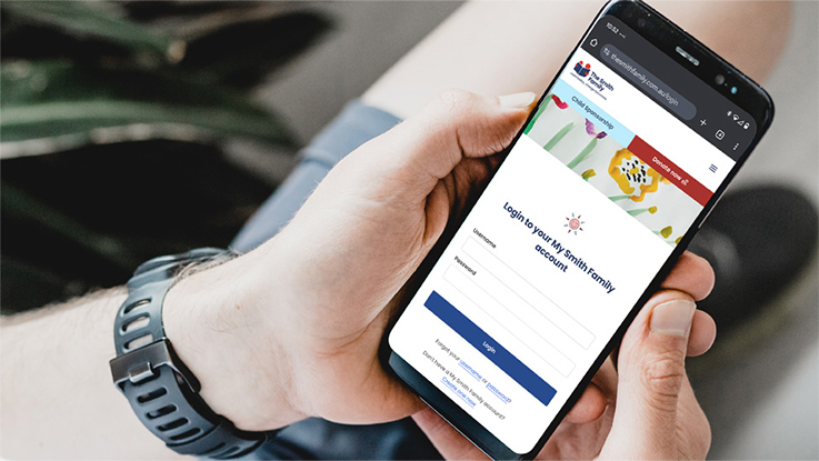 Person holding a smartphone displaying the login page for "My Smith Family" account.