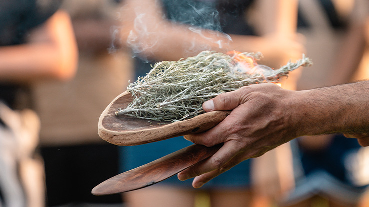 an image of hands holding wood instruments while burning vegetation