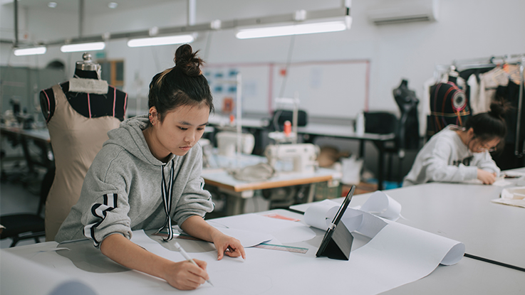 textile student working at a desk with dress behind on a  mannequin