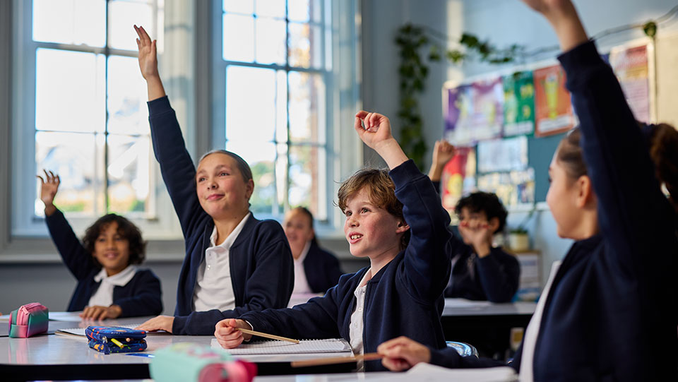 children in a classroom with their hands up