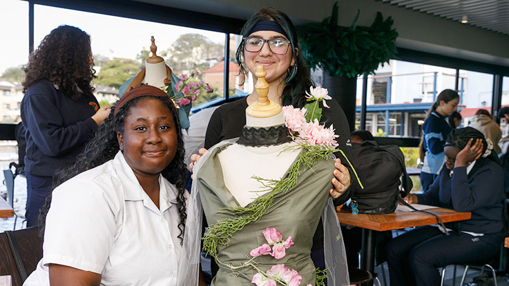 Two students display a floral dress on a mannequin during a creative arts workshop.