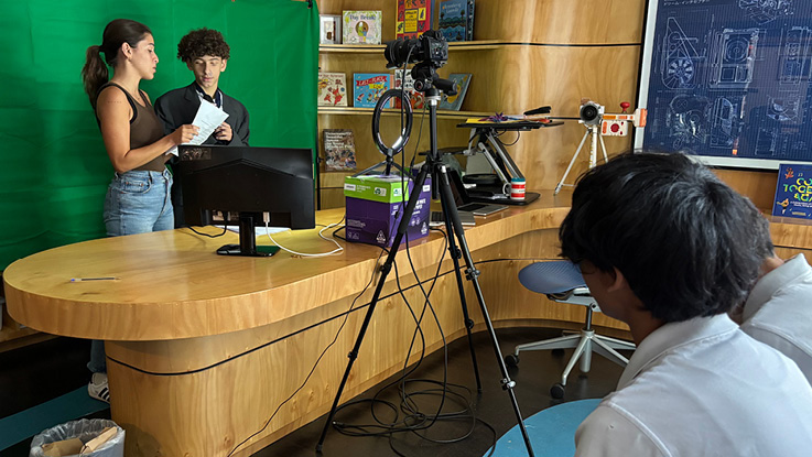 two high school students are filming and recording with a teacher supporting them