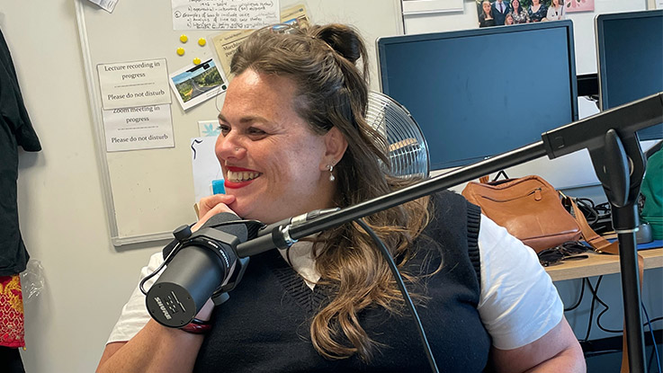 a woman wearing a white t shirt and a knit vest sitting in front of a podcast microphone