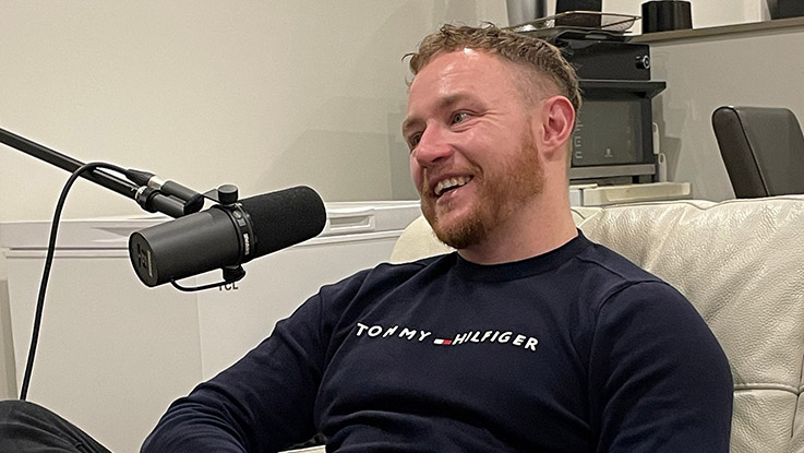 a man sitting on a white couch wearing a black sweater sitting in front of a microphone