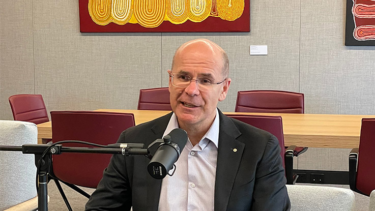 a man with glasses wearing a suit sitting in front of a podcast microphone
