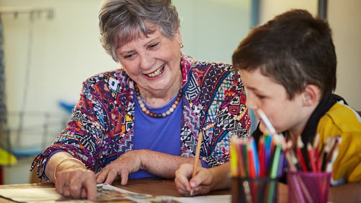 woman in colourful top helps student with homework with colourful pencils in foreground
