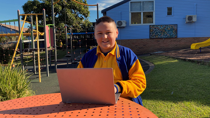 a school boy in the playground on his laptop smiling