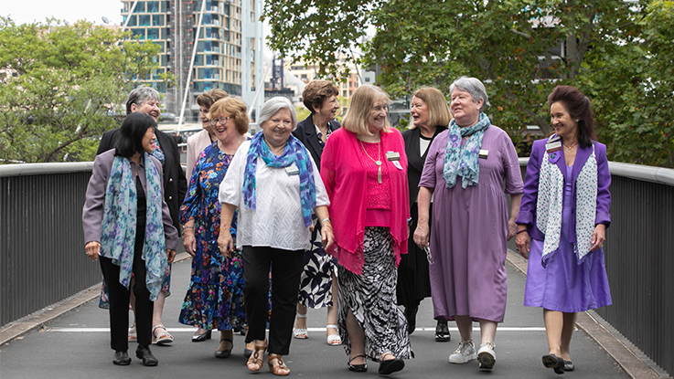 Group of older adults walking together outdoors on a city footbridge.