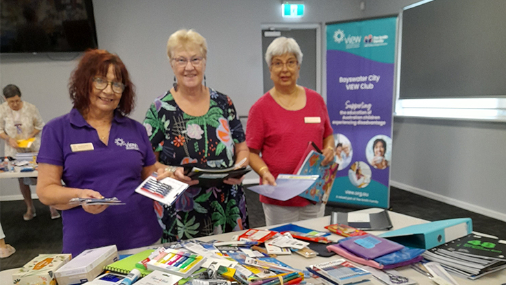 Volunteers standing behind a table of school supplies at a community event.