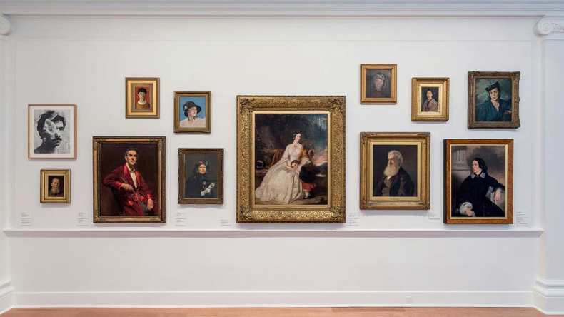 Gallery wall featuring a collection of framed portrait paintings and artworks displayed in a museum setting.